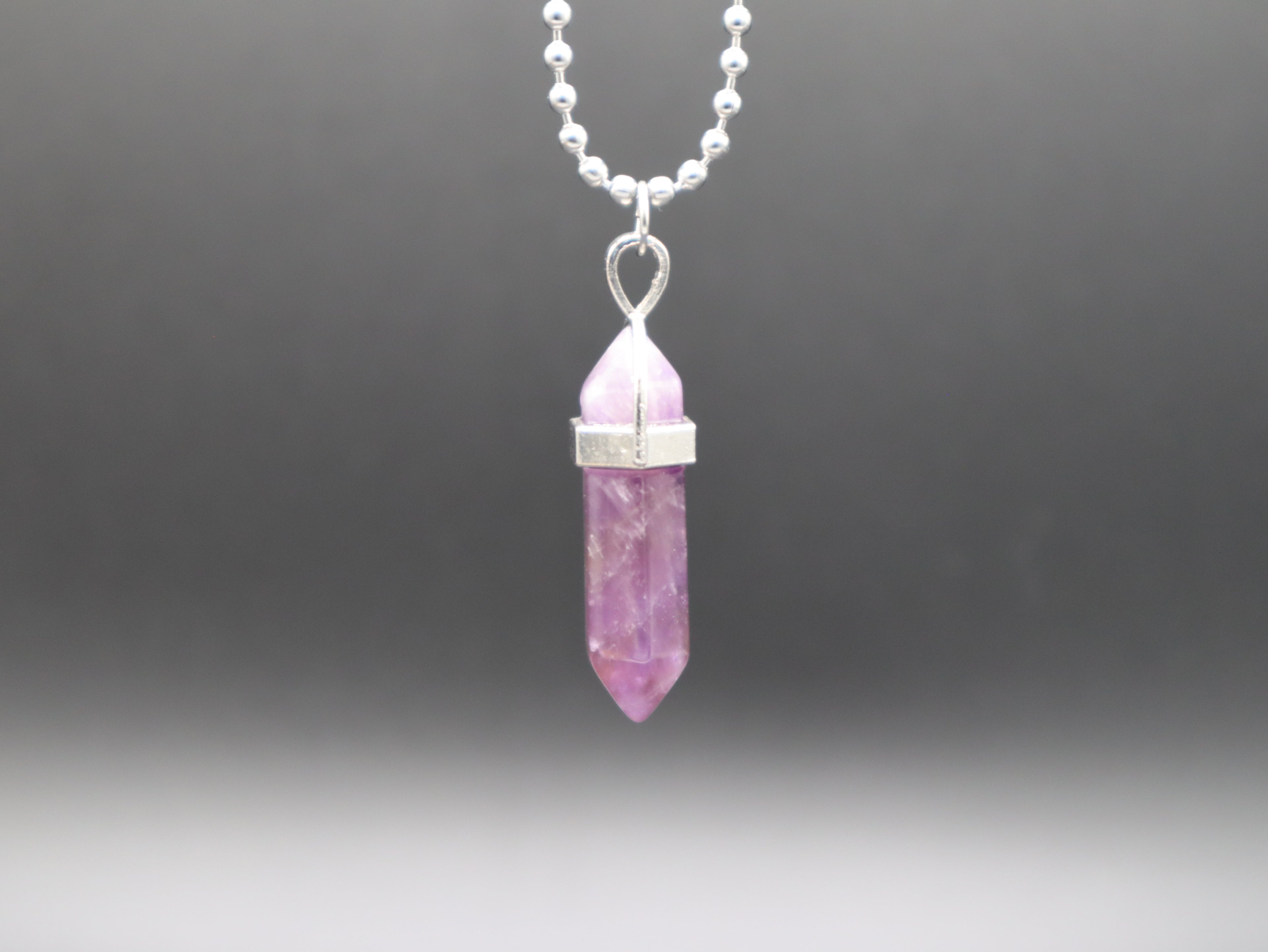 Pink crystal pendant on a silver chain against a dark gray background