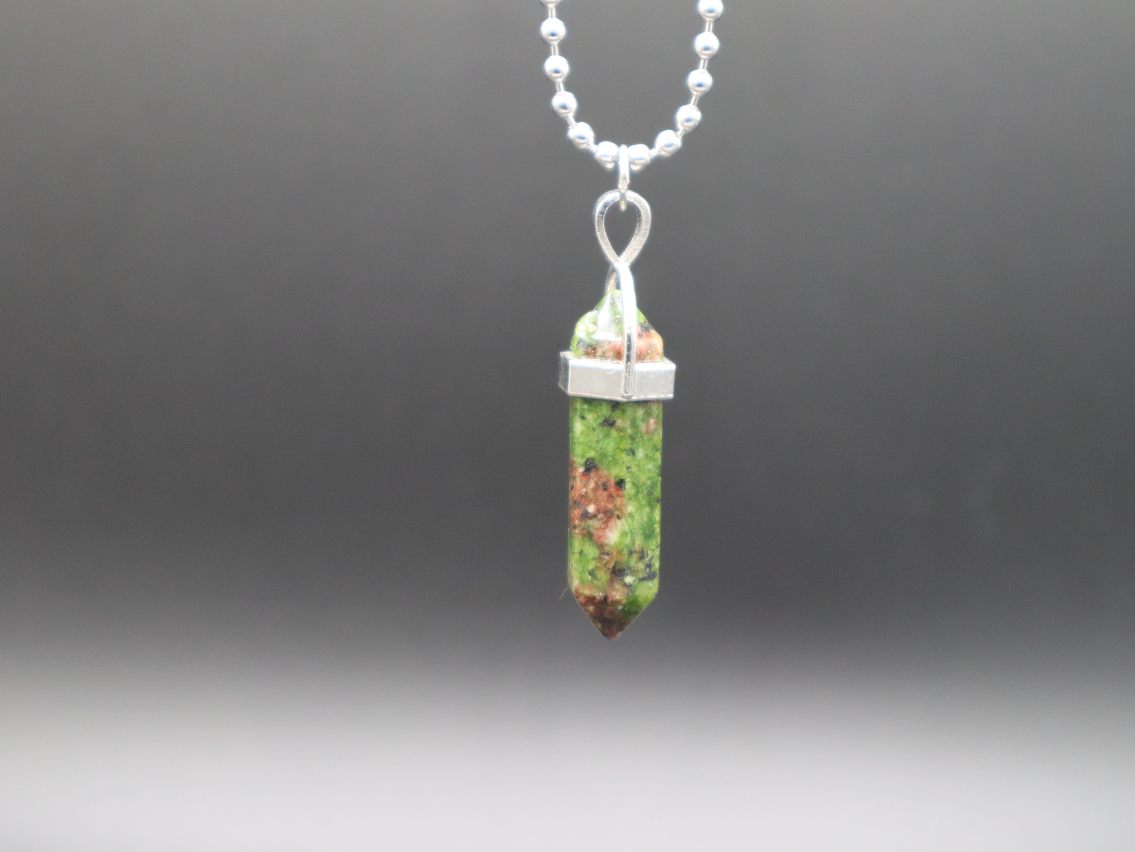 Green crystal pendant on a chain against a dark background